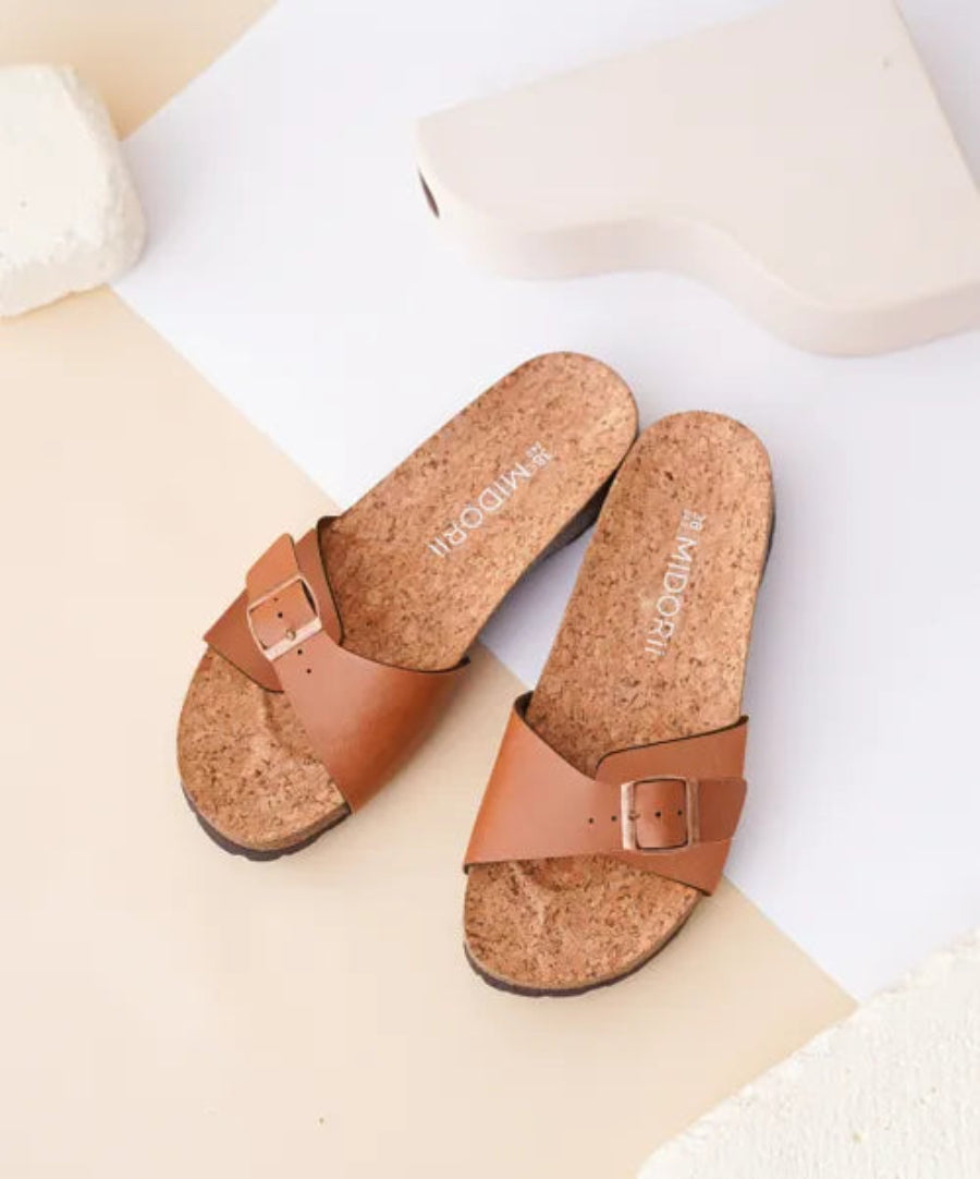 Pair of brown cork sandals with a buckle on a light background